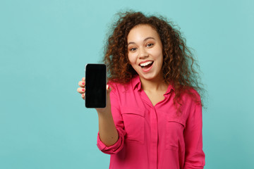Naklejka premium Excited african girl in casual clothes hold mobile phone with blank empty screen isolated on blue turquoise wall background in studio. People sincere emotions, lifestyle concept. Mock up copy space.