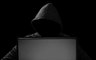 hacker with glowing mask behind notebook laptop in front of isolated black background internet...