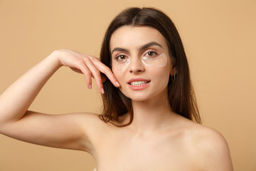 Close up half naked woman 20s with perfect skin, nude make up patches under eyes isolated on beige...