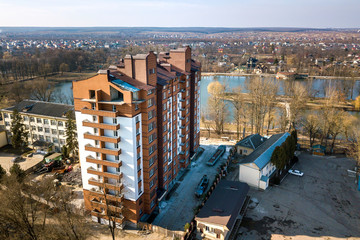 Aerial view of new tall apartment building in quiet area on background of developing city landscape under bright blue sky.