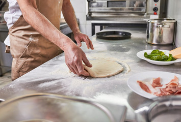 Processing of the pizza dough by the pizza maker at Italian restaurant kitchen  - obrazy, fototapety, plakaty