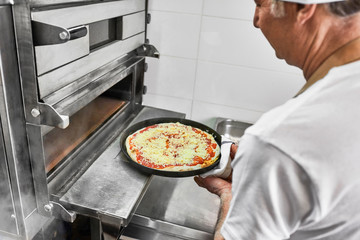Chef putting pizza into the restaurant oven 