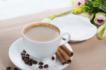 white cup of coffee on the background of scattered coffee beans and flowers