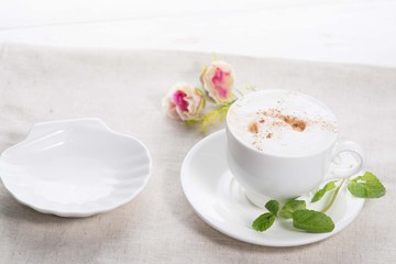 white cup of coffee on a background of scattered flower buds on a white background