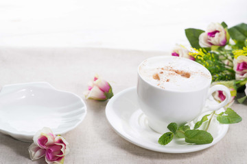 white cup of coffee on a background of scattered flower buds on a white background