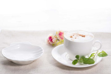 white cup of coffee on a background of scattered flower buds on a white background