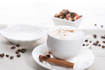 white cup of coffee on a background of scattered coffee beans on a white background