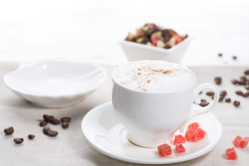 white cup of coffee on a background of scattered coffee beans on a white background