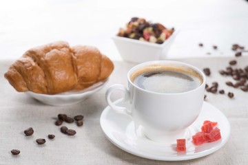 cup of coffee and a croissant on a served table with flower buds