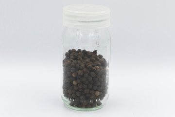 Fototapeta na wymiar Black pepper in glass storage container with white plastic lid.