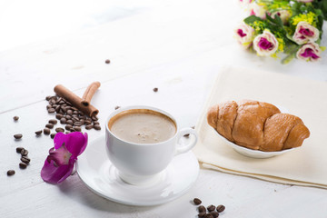 cup of coffee and a croissant on a served table with flower buds