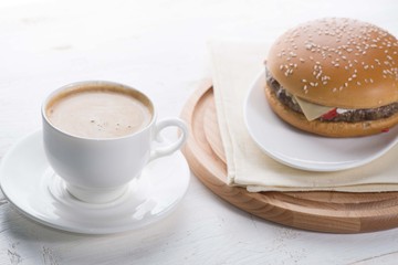 cup of coffee and burger on a served white table