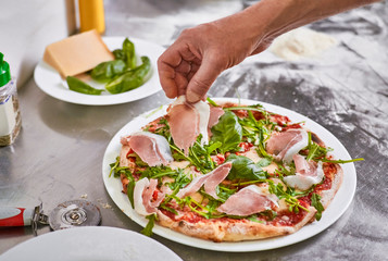 Close up hands of chef making fresh homemade traditional Italian pizza, putting ingridients