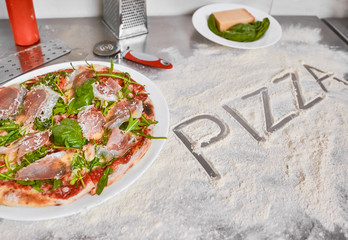Fresh baked pizza on working counter-top with word pizza written in flour