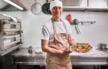 Chef holding fresh pizza in kitchen
