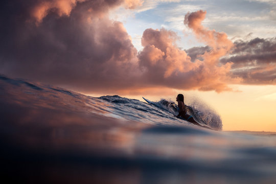 Silhouette of woman surfing in the ocean at sunset. Beautiful clouds. Vivid warm colors.