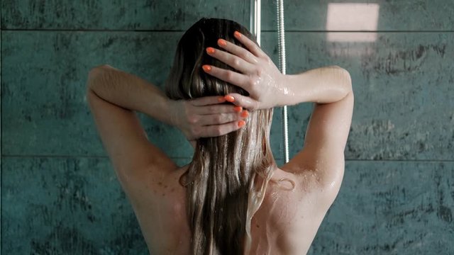Beautiful young woman blonde washes in the shower in the bathroom. Gray tile.