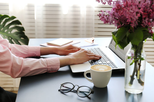 Feminine freelance workspace concept. Woman's hands typing on white laptopp with black keyboard, desk with matte blue table top. Freelance blogger writing an article. Close up, copy space for text.