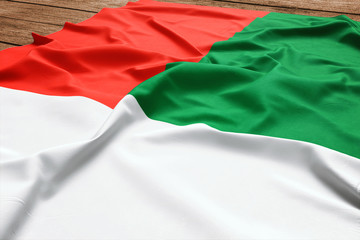 Flag of Madagascar on a wooden desk background. Silk Malagasy flag top view.