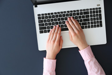 Feminine freelance workspace concept. Woman's hands typing on white laptopp with black keyboard, desk with matte blue table top. Freelance blogger writing an article. Close up, copy space for text.