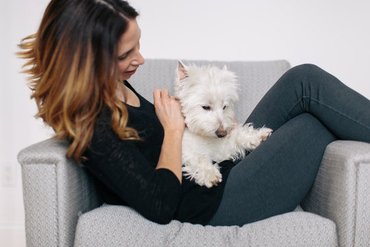 Beautiful woman sitting on a chair snuggling her small white dog