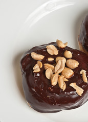 top view, close up of a baked, yeast donut covered with chocolate frosting and salted peanuts in a deep, square, ceramic dish