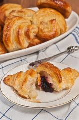 top view, close distance of a freshly baked, homemade croissant, ripped open  with raspberry filling  on a round, white plate with an artisan butterknife and an oval, white plate with more croissants