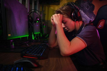 Professional young caucasian gamer playing online on his PC. He upset because of losing the game
