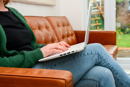 Trendy Woman At Home Using A Laptop Whilst Sitting On Leather Couch At Home