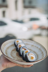 A stylish young smiling girl poses for a photo and holding in her hand a plate of rolls and chopsticks in the other hand. Appetizing advertising photography for restaurant, sushi bar, delivery
