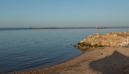 deserted dirty beach on the background of a long old pier at sunset