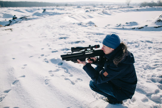 Side view portrait of the man sitting on snow with gun