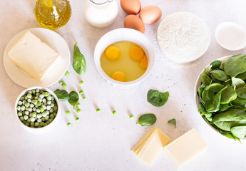 Ingredients for making tart, quiche, pie or cake - flour, eggs, milk, olive oil, spinach, green pea, cheese and butter. Food background. Copy space.
