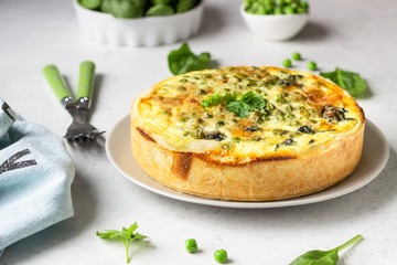 Spinach and green pea quiche, tart or pie with fresh ingredients for baking. Light grey background,...