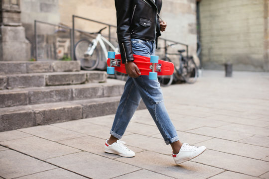 Cool woman holding a red skateboard in the city.