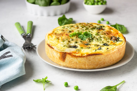 Spinach and green pea quiche, tart or pie with fresh ingredients for baking. Light grey background, copy space. 