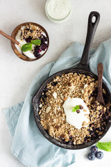 Oatmeal crumble in cast iron pan with fresh blueberry and natural yogurt. Healthy food concept. 
