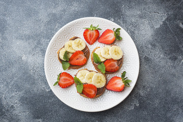 Delicious sandwiches with chocolate nougat, strawberry and banana. Concept of Breakfast. Dark concrete background.
