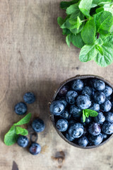 Freshly picked blueberries in wooden bowl. Juicy and fresh blueberries with mint on wooden table. Bilberry on rustic background. Blueberry antioxidant. Concept for healthy eating and nutrition. 