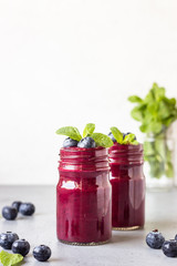 Delicious blueberry smoothie with fresh berries and mint in glass jars. Summer healthy drink. Grey stone background. Copy space.