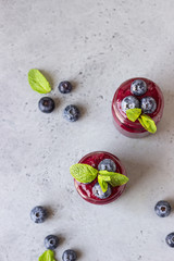 Delicious blueberry smoothie with fresh berries and mint in glass jars. Summer healthy drink. Grey stone background. Copy space.