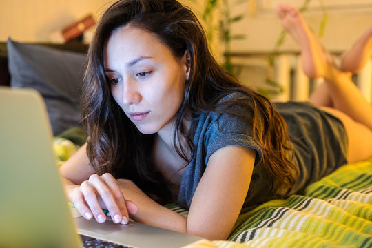 Young woman browsing on her laptop at a bed in a  bedroom