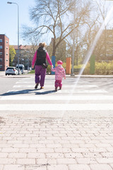 Mom and daughter cross the road at a pedestrian crossing. Sunny spring day and family in the city