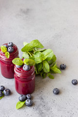 Delicious blueberry smoothie with fresh berries and mint in glass jars. Summer healthy drink. Grey stone background. Copy space.