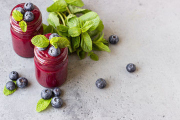 Delicious blueberry smoothie with fresh berries and mint in glass jars. Summer healthy drink. Grey stone background. Copy space.