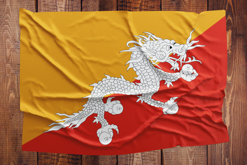 Flag of Bhutan on a wooden table background. Wrinkled Bhutanese flag top view.