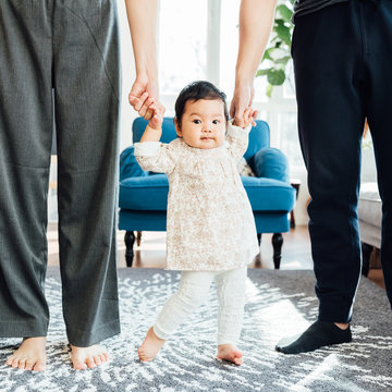Adorable girl learning walk with her parents help