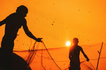 Anonymous, unrecognizable, silhouetted fisherman on the beach shore using fishing net during beautiful, golden sunset