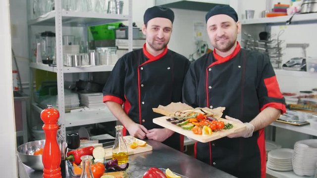 Restaurant kitchen. Two men chefs finished serving the dish, taking it on the hands and doing a bellissimo gesture