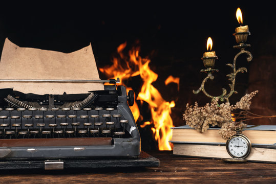Typewriter, Stack Of Books, Burning Candle On A Writer Table On A Burning Fire Background.